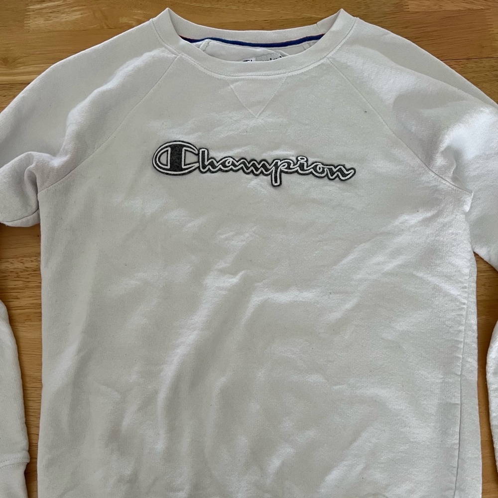 small, white, Champion crewneck with gray and white logo on the front